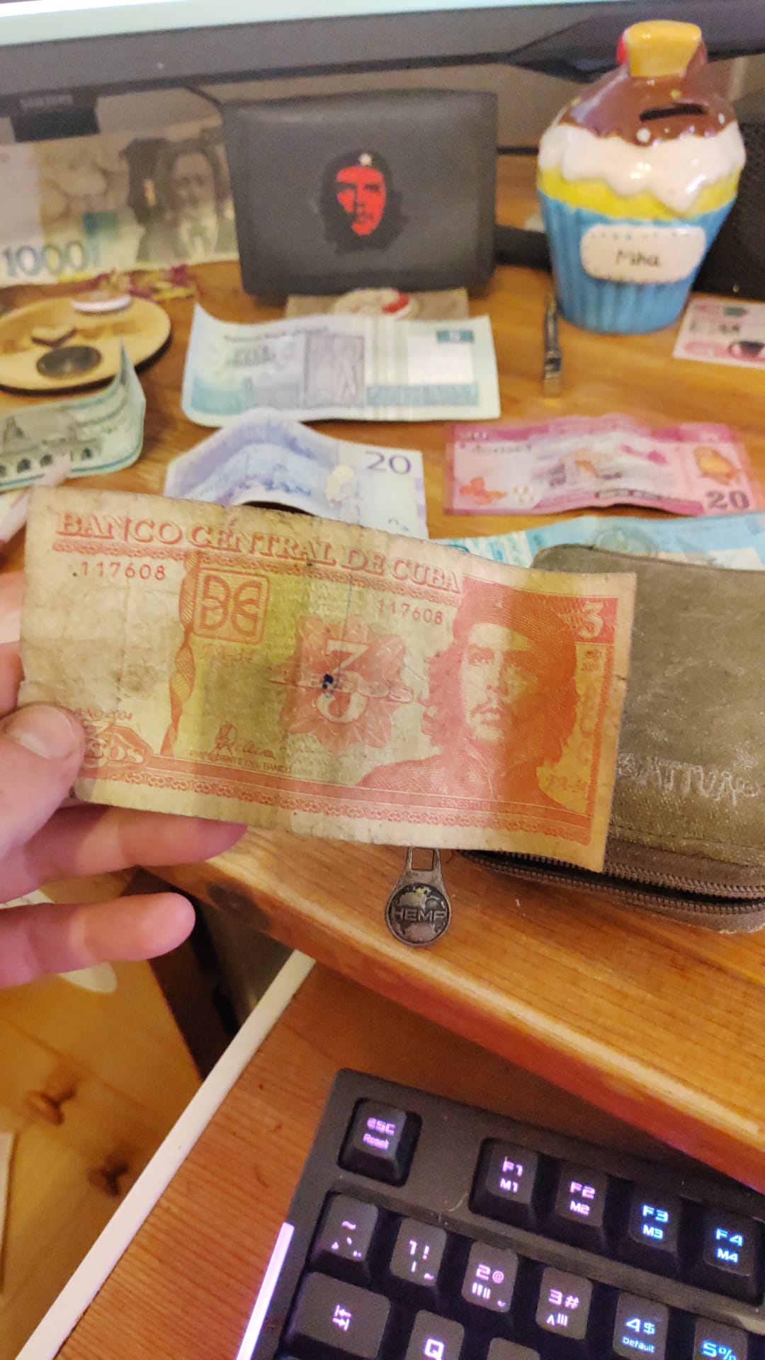A worn orange Cuban 3 pesos banknote from Banco Central de Cuba featuring Che Guevara, held above a Sativa hemp wallet.
